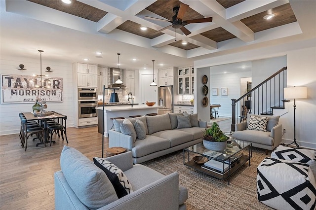 living room with coffered ceiling, hardwood / wood-style flooring, beam ceiling, and ceiling fan with notable chandelier