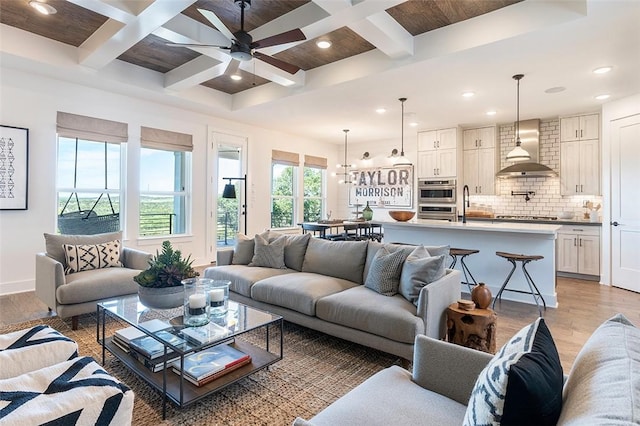 living room with beamed ceiling, coffered ceiling, ceiling fan, and light hardwood / wood-style flooring