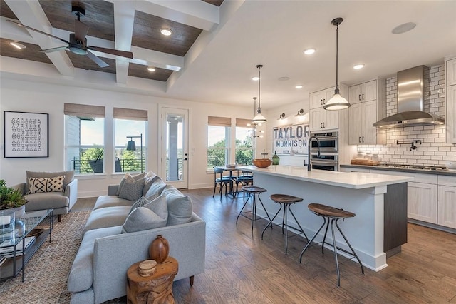 living room with dark wood-type flooring, ceiling fan, coffered ceiling, and beamed ceiling