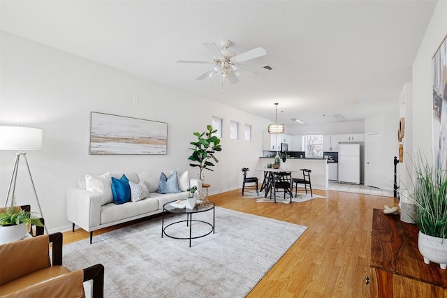 living area featuring light wood-style flooring, visible vents, ceiling fan, and baseboards