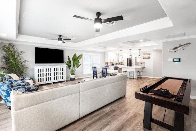 living room featuring crown molding, ceiling fan, a tray ceiling, and light wood-type flooring