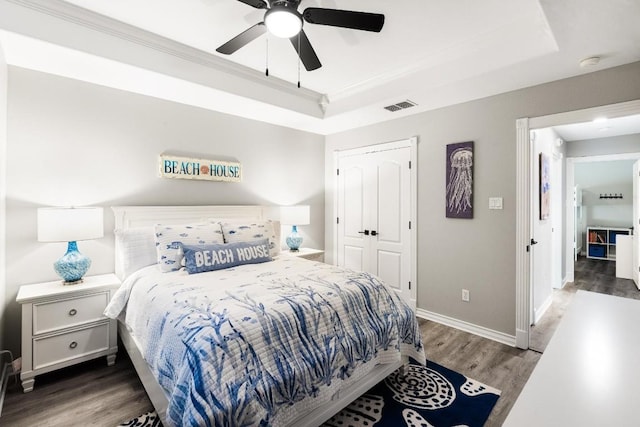 bedroom with dark wood-type flooring, crown molding, a tray ceiling, a closet, and ceiling fan