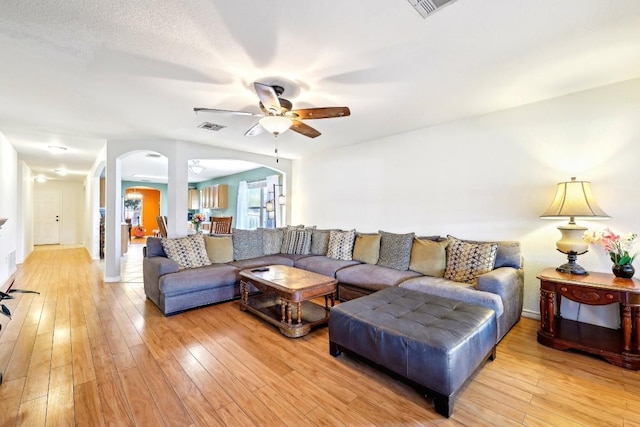 living room with light wood-type flooring, arched walkways, visible vents, and a ceiling fan