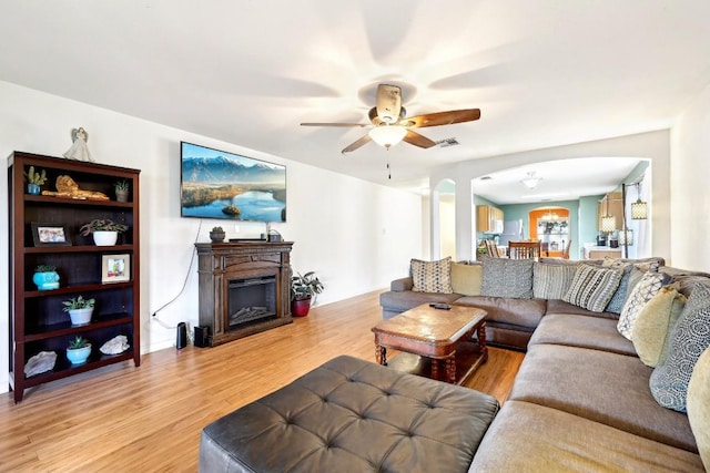 living room with arched walkways, ceiling fan, a fireplace, visible vents, and light wood-style floors