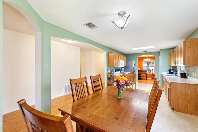 dining room featuring arched walkways, a chandelier, visible vents, and baseboards