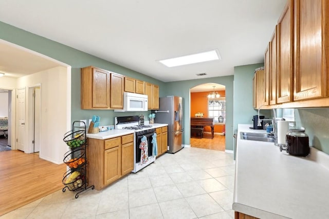 kitchen with white appliances, light tile patterned floors, visible vents, arched walkways, and light countertops