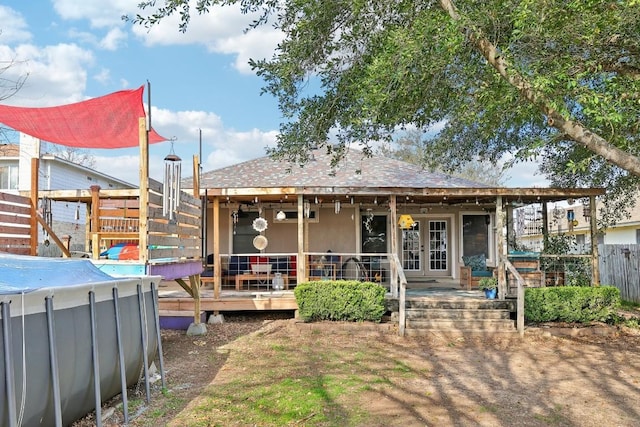 rear view of house with a pool, french doors, and fence