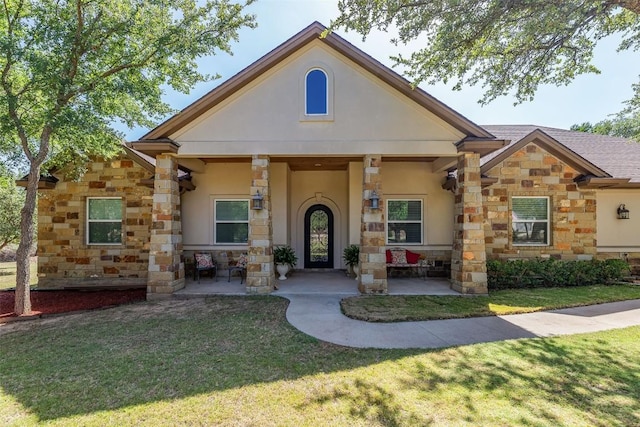 view of front of property with covered porch, a shingled roof, stone siding, stucco siding, and a front yard