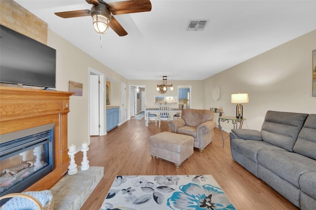 living room with ceiling fan with notable chandelier and light hardwood / wood-style flooring