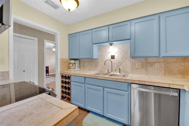 kitchen featuring blue cabinetry, stainless steel dishwasher, sink, and backsplash