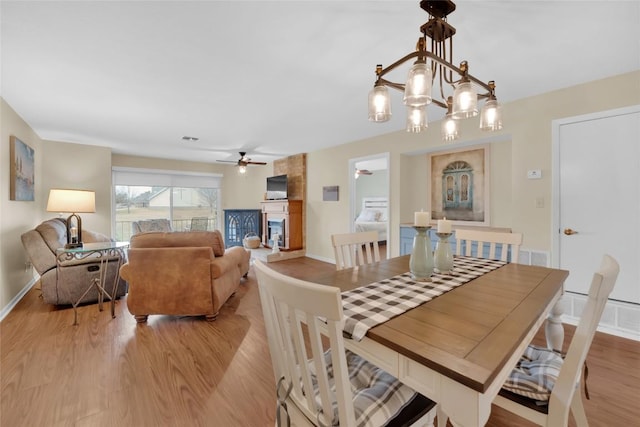 dining area with ceiling fan, a fireplace, and light wood-type flooring