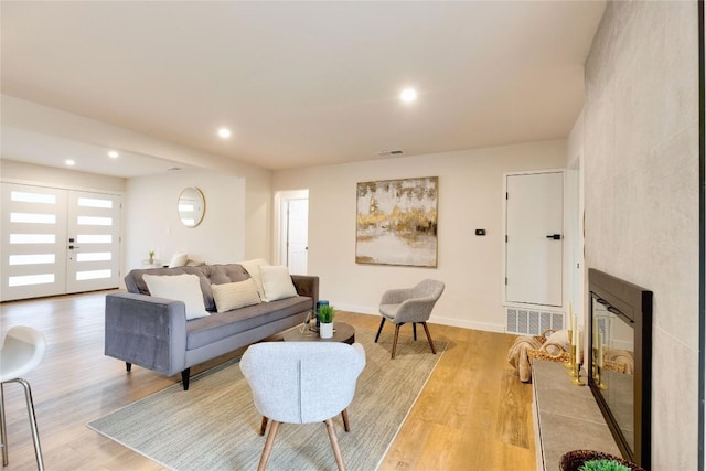 living room with light hardwood / wood-style floors, a premium fireplace, and french doors