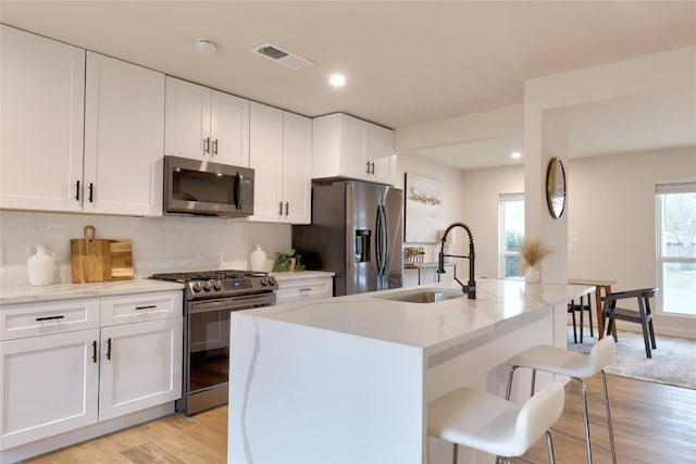 kitchen with stainless steel appliances, a breakfast bar, sink, white cabinetry, and a kitchen island with sink