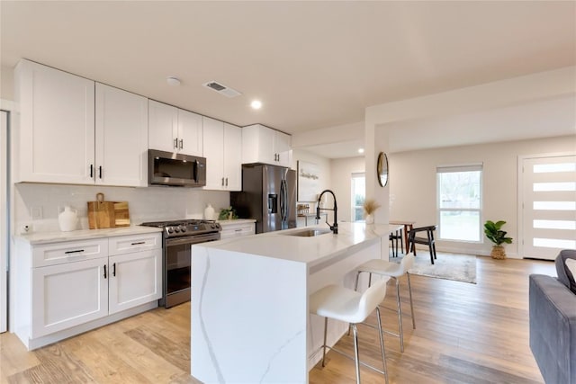 kitchen with appliances with stainless steel finishes, sink, white cabinetry, and a kitchen island with sink