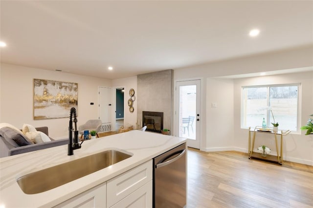 kitchen featuring light hardwood / wood-style flooring, sink, dishwasher, a large fireplace, and white cabinets