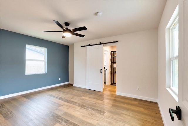 unfurnished bedroom featuring ceiling fan, a barn door, and light hardwood / wood-style floors