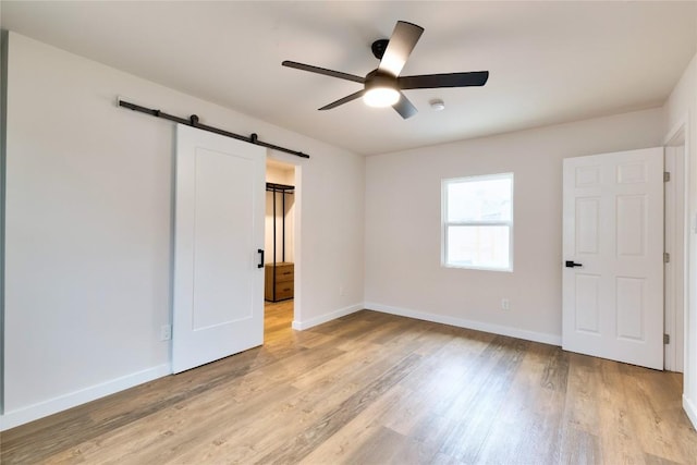 unfurnished bedroom featuring light hardwood / wood-style flooring, ceiling fan, and a barn door