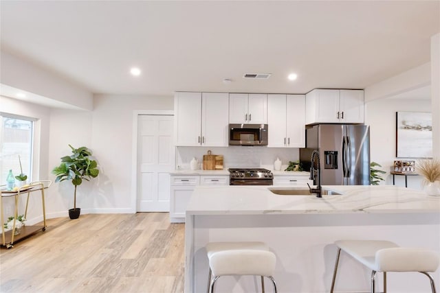 kitchen featuring white cabinetry, appliances with stainless steel finishes, sink, and light stone countertops