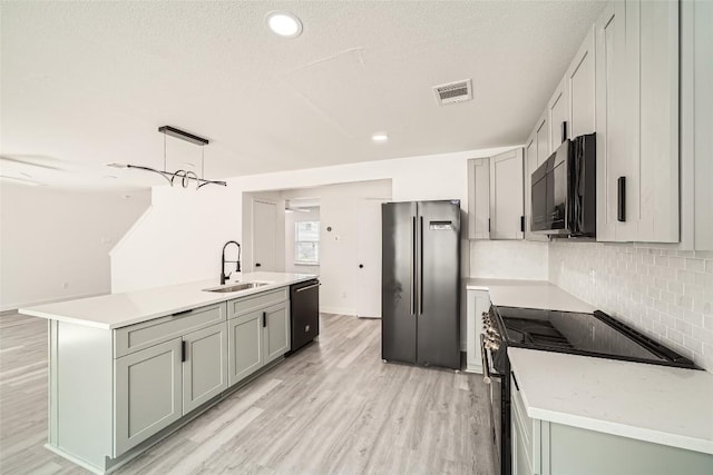 kitchen with sink, hanging light fixtures, black appliances, a center island with sink, and light wood-type flooring