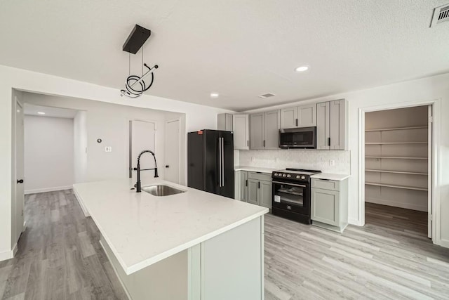 kitchen featuring pendant lighting, sink, black appliances, and an island with sink