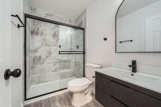 bathroom featuring vanity, wood-type flooring, a shower with door, and toilet