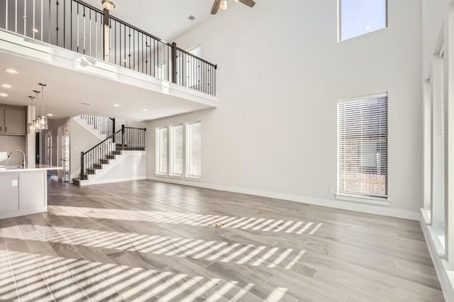 unfurnished living room featuring ceiling fan, sink, light hardwood / wood-style floors, and a high ceiling