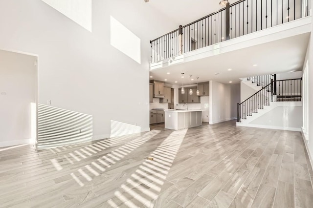 155 Cyrus Milton Dr, Buda, TX 78610 - unfurnished living room featuring a towering ceiling, a sink, stairway, light wood finished floors, and baseboards