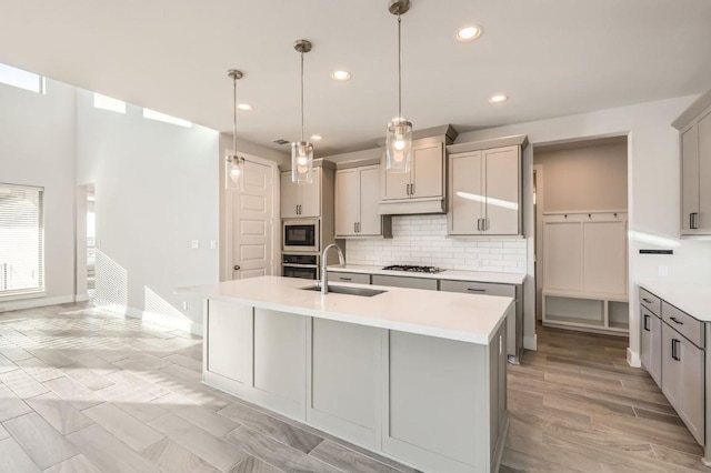 kitchen with sink, gray cabinets, appliances with stainless steel finishes, an island with sink, and decorative light fixtures