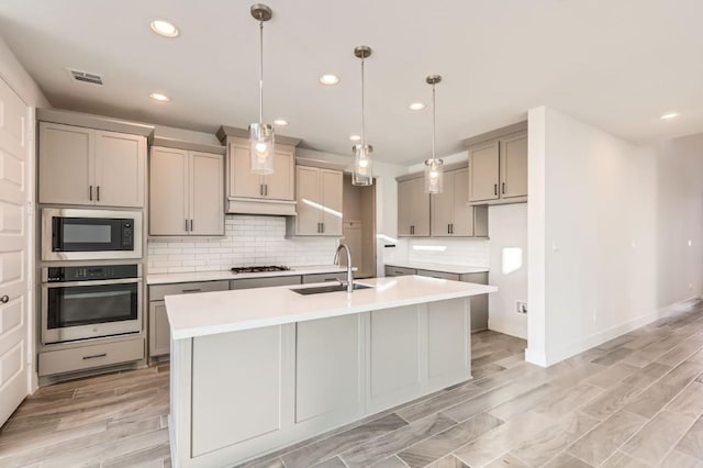 kitchen with tasteful backsplash, appliances with stainless steel finishes, pendant lighting, and a center island with sink