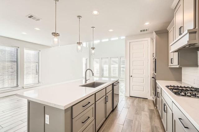 kitchen featuring gray cabinets, appliances with stainless steel finishes, pendant lighting, an island with sink, and sink