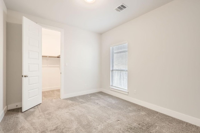 unfurnished bedroom with a spacious closet, light colored carpet, and a closet