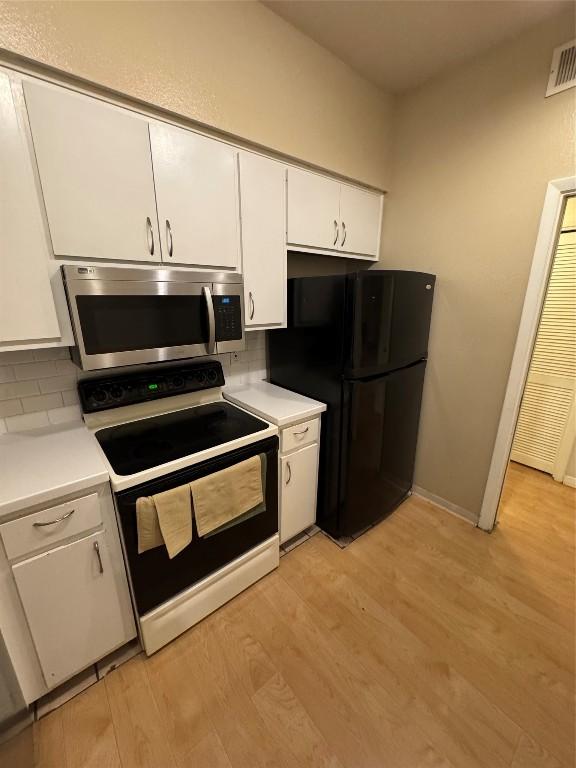 kitchen featuring light hardwood / wood-style flooring, white cabinetry, backsplash, black refrigerator, and range with electric stovetop