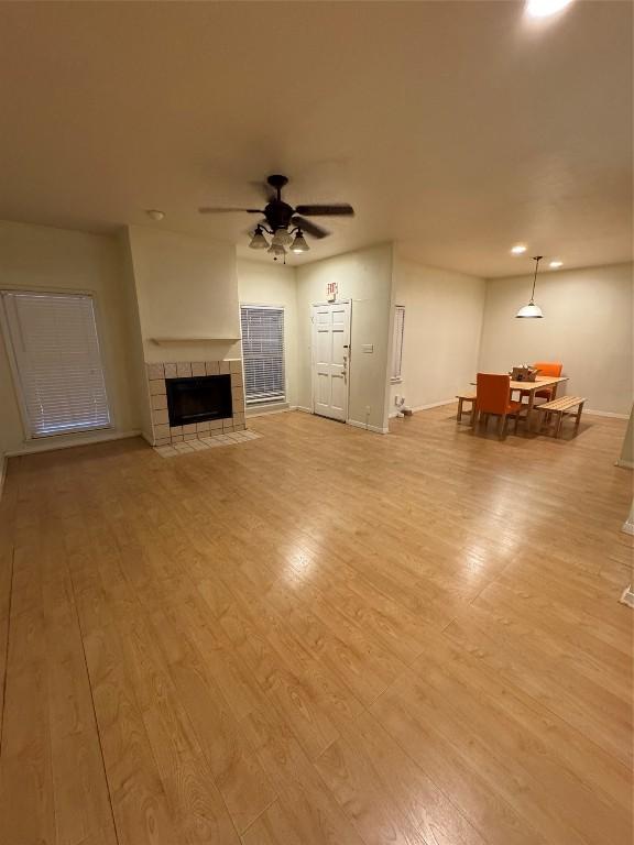 unfurnished living room featuring ceiling fan, a tiled fireplace, and light wood-type flooring