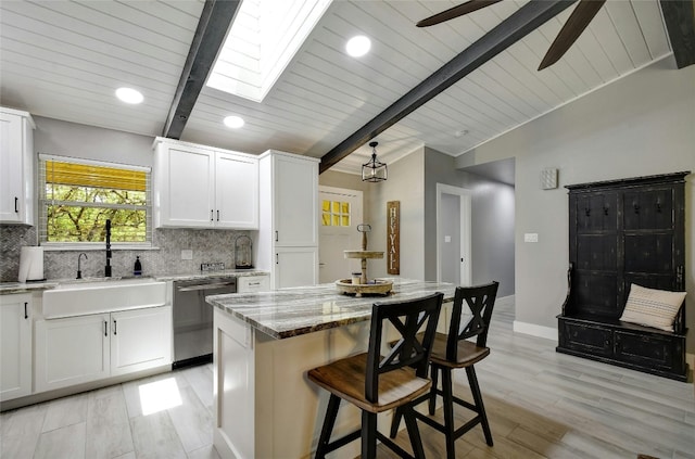 kitchen with dishwasher, a kitchen breakfast bar, light stone countertops, white cabinets, and a kitchen island