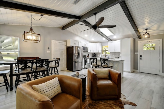 living room featuring ceiling fan with notable chandelier, plenty of natural light, lofted ceiling with beams, and light wood-type flooring