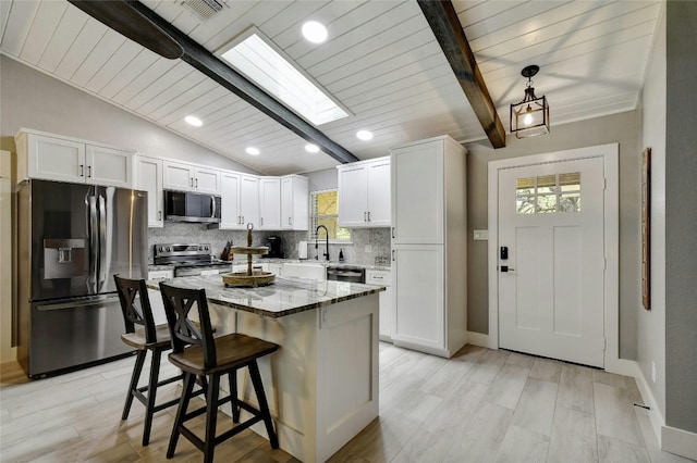 kitchen with stone counters, white cabinetry, appliances with stainless steel finishes, a kitchen breakfast bar, and a center island