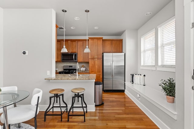 kitchen featuring hanging light fixtures, backsplash, stainless steel appliances, light hardwood / wood-style floors, and kitchen peninsula