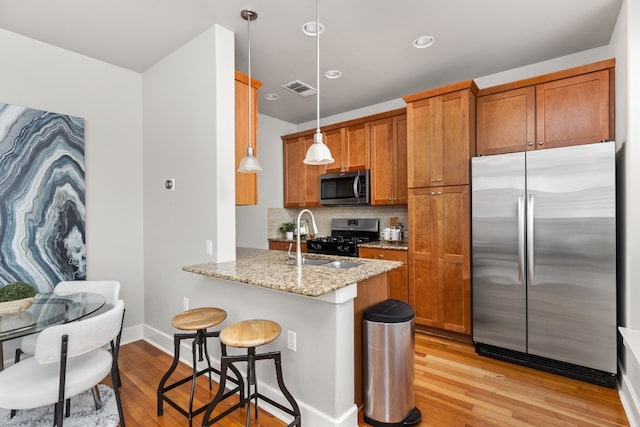 kitchen with sink, appliances with stainless steel finishes, hanging light fixtures, light stone countertops, and kitchen peninsula