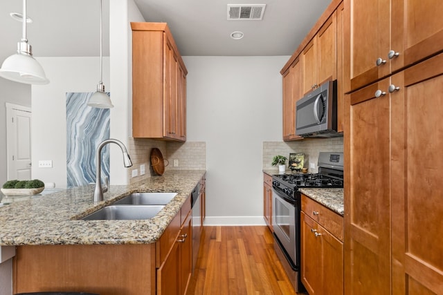 kitchen featuring pendant lighting, sink, appliances with stainless steel finishes, light stone counters, and light hardwood / wood-style floors