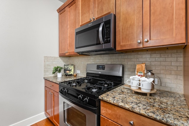 kitchen with appliances with stainless steel finishes, light stone countertops, light hardwood / wood-style floors, and backsplash