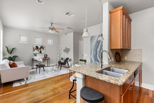 kitchen featuring sink, hanging light fixtures, tasteful backsplash, wood-type flooring, and light stone countertops