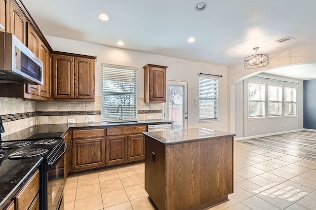 kitchen with sink, appliances with stainless steel finishes, a healthy amount of sunlight, a kitchen island, and light tile patterned flooring