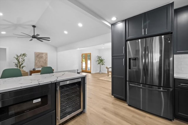 kitchen featuring vaulted ceiling, wine cooler, stainless steel fridge, light stone counters, and light wood-type flooring