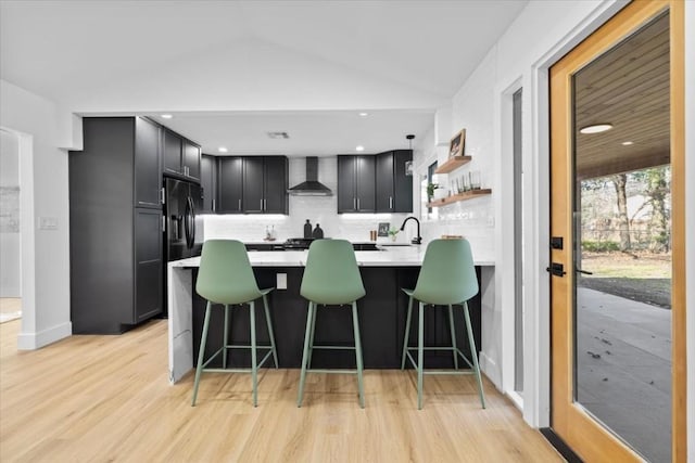 kitchen featuring wall chimney exhaust hood, a kitchen breakfast bar, kitchen peninsula, and decorative backsplash