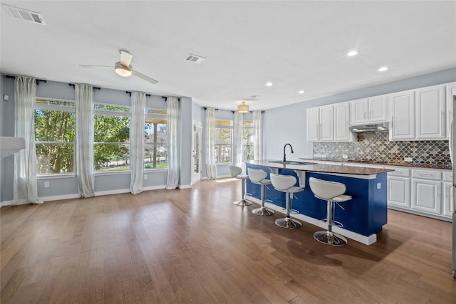 kitchen featuring a breakfast bar, sink, white cabinetry, an island with sink, and decorative backsplash