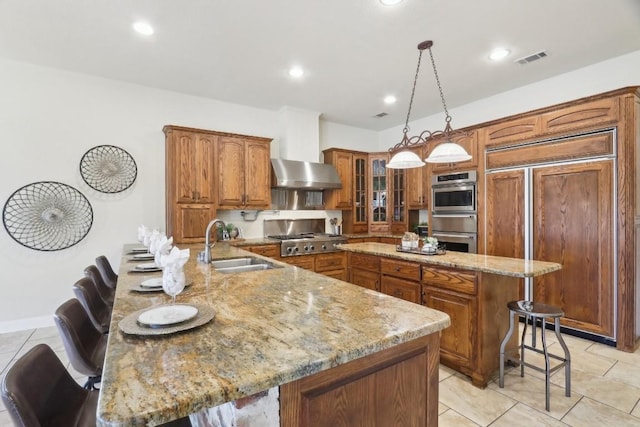 kitchen featuring a kitchen breakfast bar, a center island, visible vents, wall chimney exhaust hood, and brown cabinetry