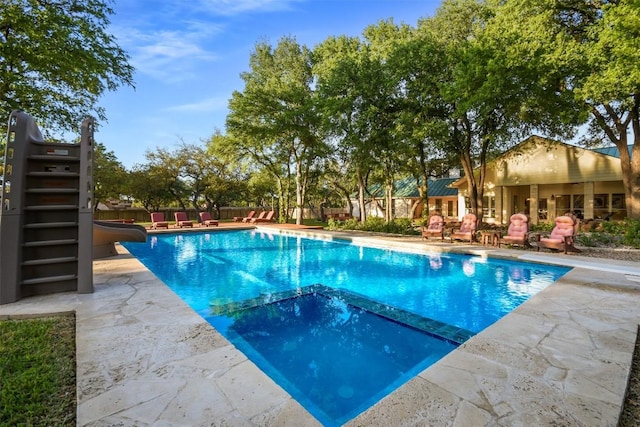 view of swimming pool with a pool with connected hot tub, a water slide, fence, and a patio area