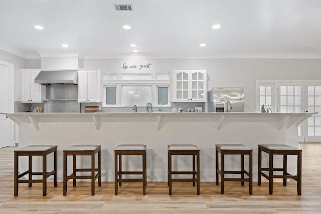 kitchen featuring white cabinetry, stainless steel fridge, a breakfast bar, and wall chimney range hood