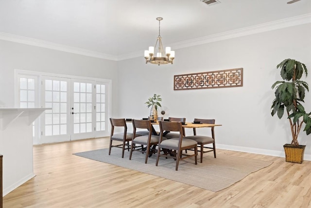 dining space featuring french doors, ornamental molding, a chandelier, and light hardwood / wood-style floors