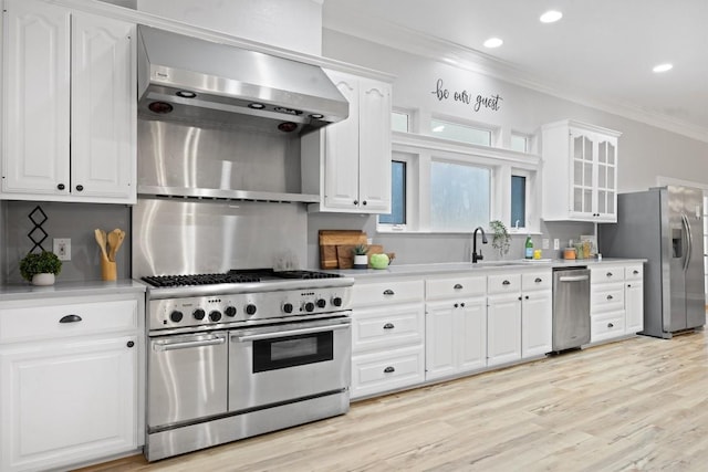 kitchen featuring crown molding, stainless steel appliances, wall chimney exhaust hood, and white cabinets